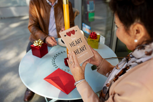 A woman sitting at a table, smiling while holding a heart-shaped card in her hands.
