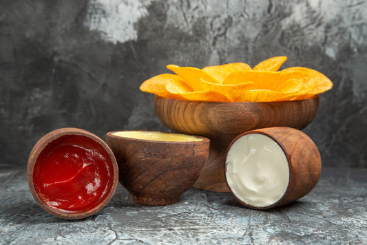 3 types of different dips next to a bowl of golden chips on a casual dining table.